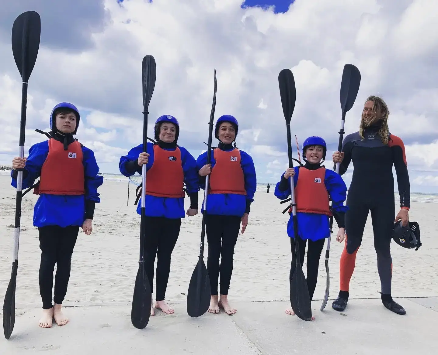 Brandingkajakken groep met peddels en zwemvesten naast een instructeur op het strand.
