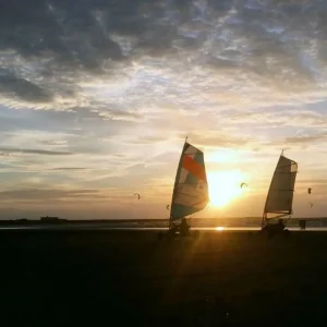 Twee blokarts rijden over het strand tijdens een teambuilding activiteit, met een prachtige ondergang van de zon op de achtergrond