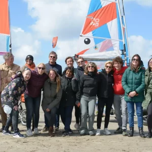 Groep collega's poseert samen voor de foto na een geslaagd blokarten evenement op het strand, lachend en genietend van hun teambuilding ervaring.