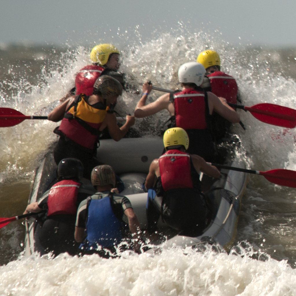 Groep collega's die door de branding proberen te komen tijdens het raften als onderdeel van een teambuilding evenement bij Outstanding