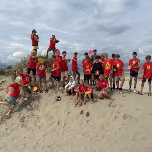 Groep kinderen staat op een duintop tijdens de discgolf activiteit bij het Outstanding zomerkamp, klaar om hun schoten te maken te midden van de natuur.